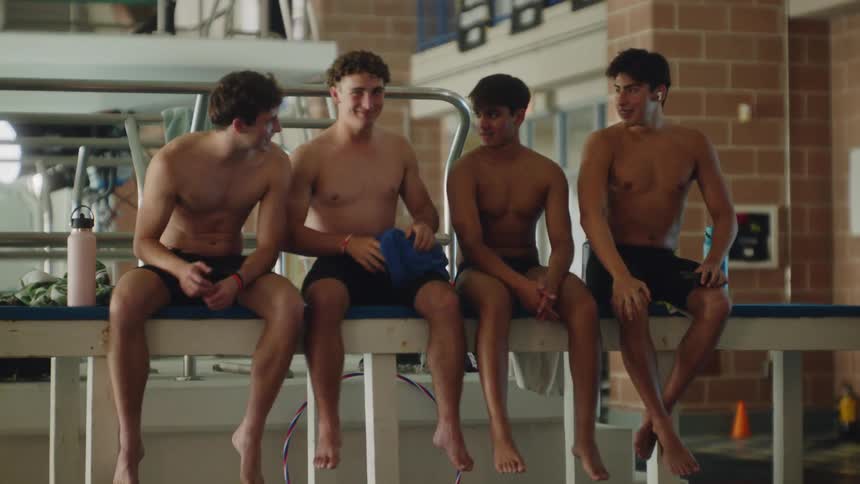 Four teenage swimmers sitting shirtless talking