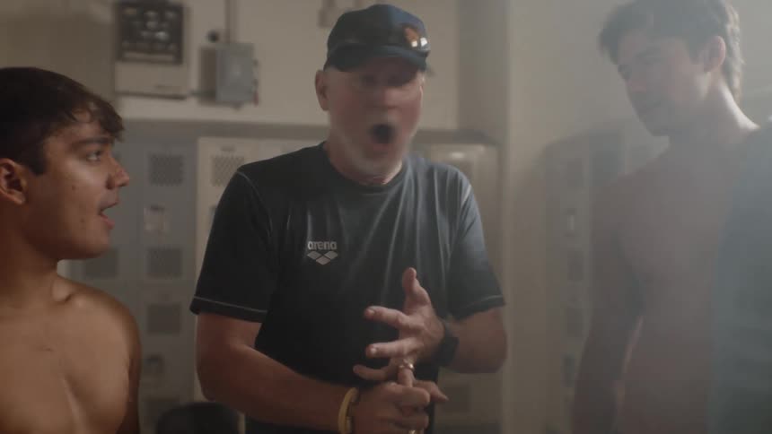 A coach delivers a pep talk to a group of young athletes in a locker room
