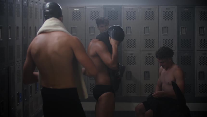 Group of young male swimmers in a locker room talking and getting ready