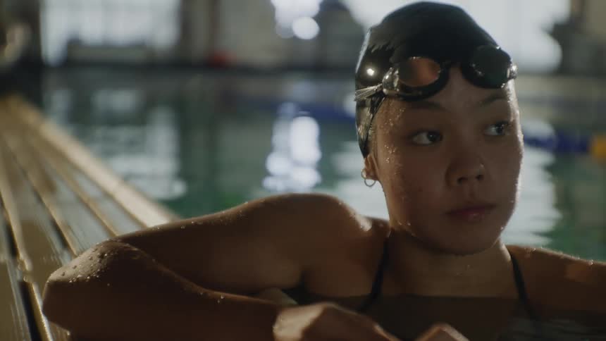 Asian woman sits in the water at the edge of the pool