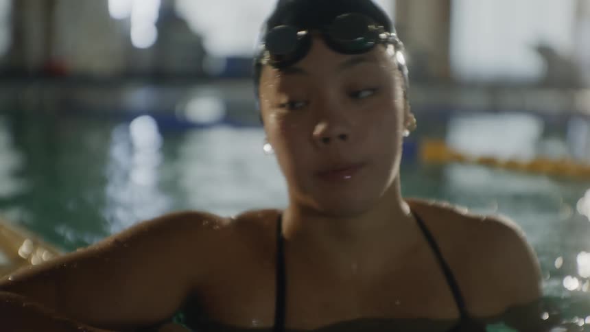 Teenage girl coming out of the water towards the corner of the pool taking off her swimming goggles