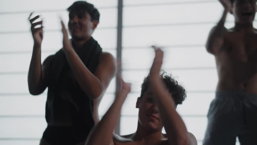 A group of young shirtless teenagers stands up clapping