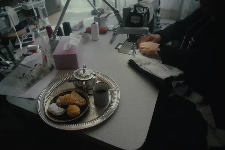 Tray of pastries and coffee sit on a table near a woman using a sewing machine