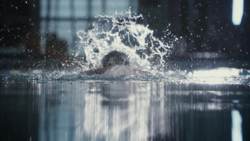 A swimmer in propels through a pool water splashing around as their arm cuts through the water