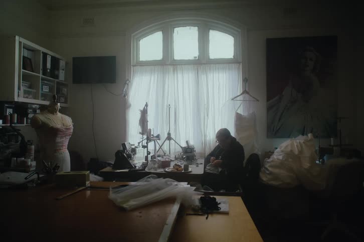 A seamstress is fitting a dress in a cluttered dimly lit workshop