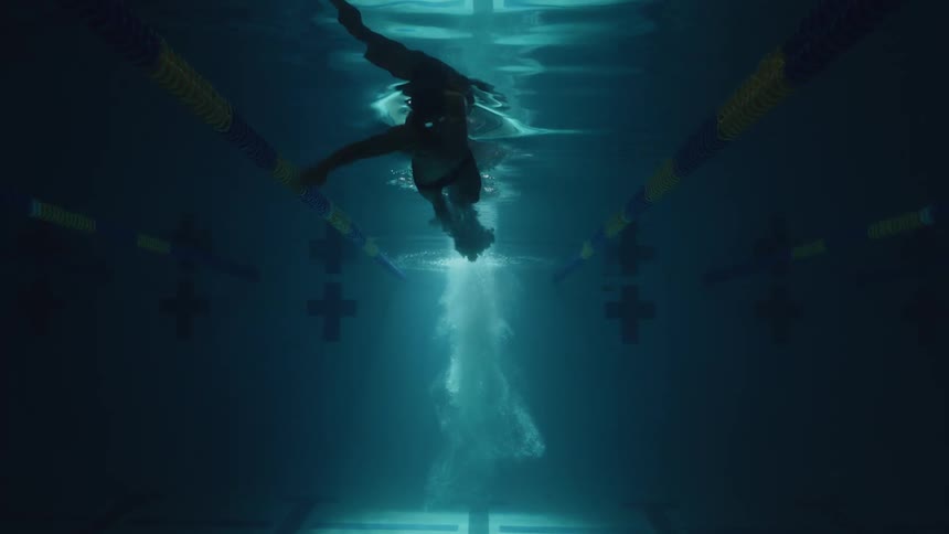 Underwater footage captures a person swimming in an olympic pool with light penetrating the water from above