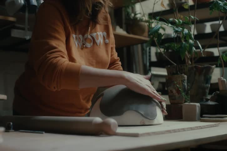 A sculptor shapes a piece of clay over a small dome over a workbench