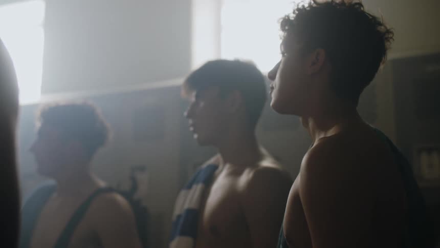 A man is talking to some shirtless boys in a bathroom with cabinets behind it