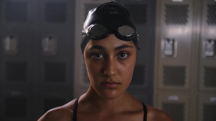 A young woman in swimming gear standing in a locker room looking focused