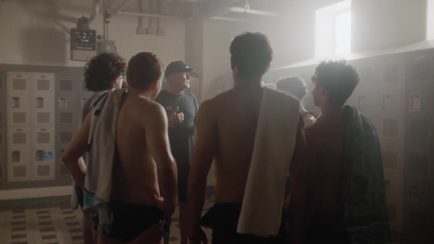 A coach delivers a pep talk to a group of young athletes in a locker room