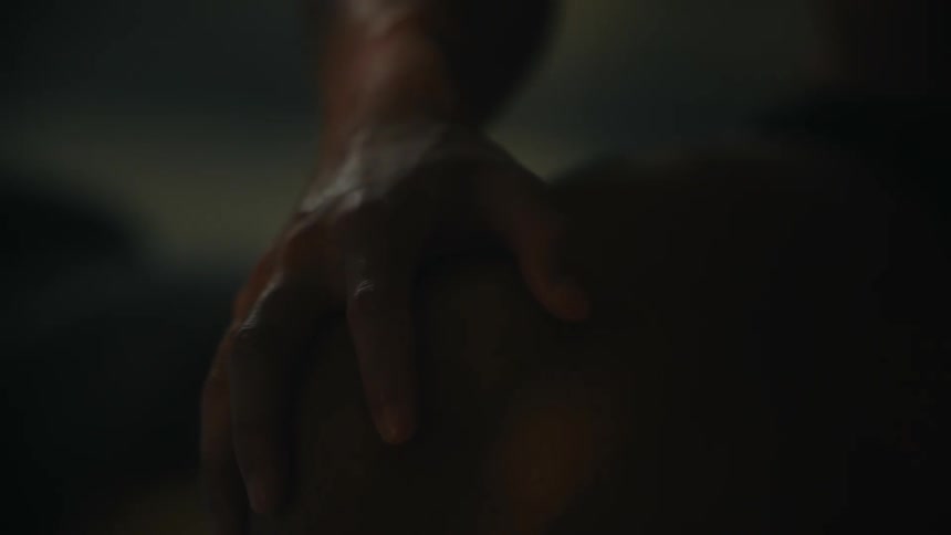 A hand rests over a leg in a dimly lit room cast under moving shadows