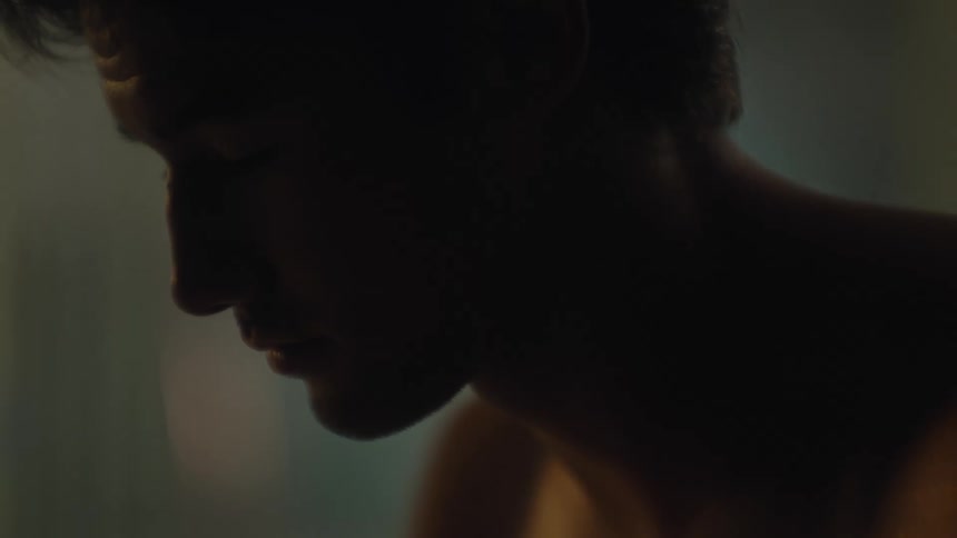 A shirtless man has his eyes closed and natural light hits his face