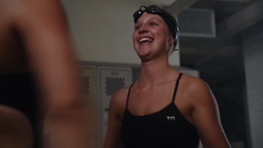 Two swimmers talk and stretch in the locker room