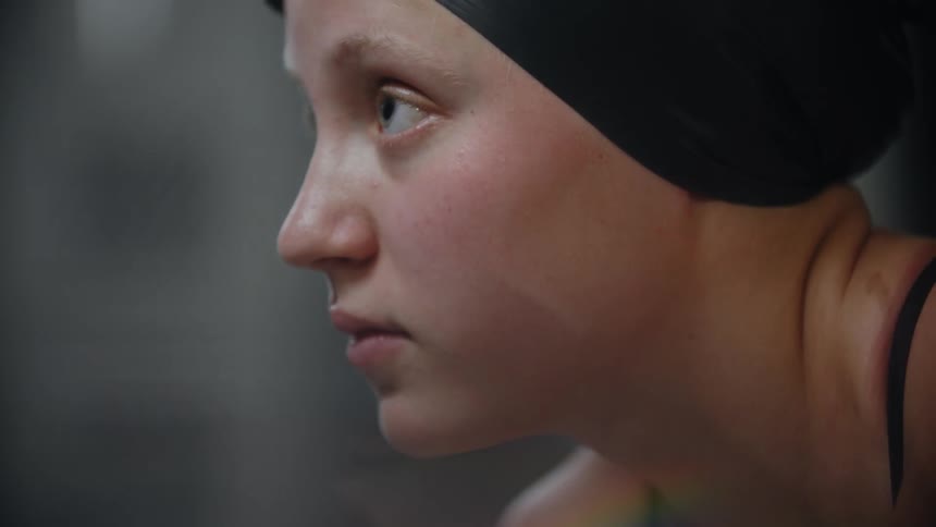 The face of a woman with a swimming cap and goggles is looking down nodding her head in confirmation tones and then looking forward