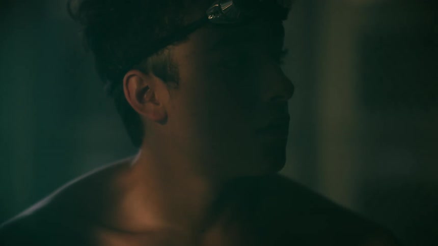 Male swimmer sits in dimly lit area looking downcast