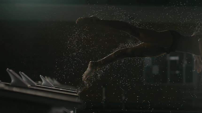 A male wearing a racing suit and skull cap dives into an indoor pool