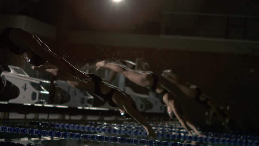 Swimmers diving into a pool illuminated by ambient light