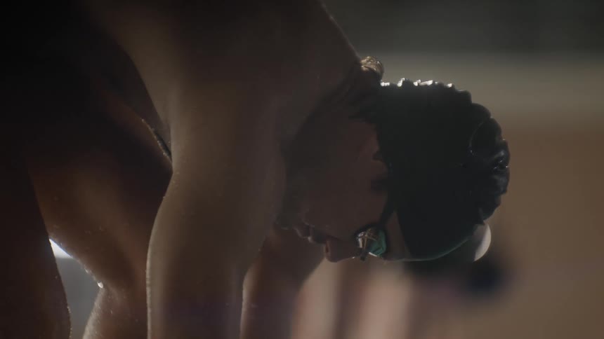 A male wearing a swim cap dives into a pool beside another person