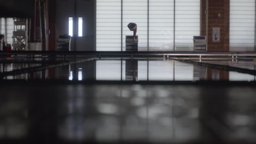 A swimmer poised on a starting block at the edge of a pool jumps in and dives