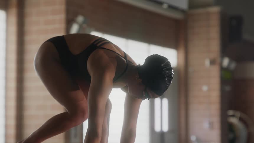 A swimmer poised on a starting block at the edge of a pool ready to jump in and dive