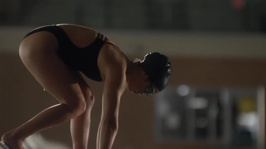 A swimmer poised on a starting block at the edge of a pool jumps in and dives