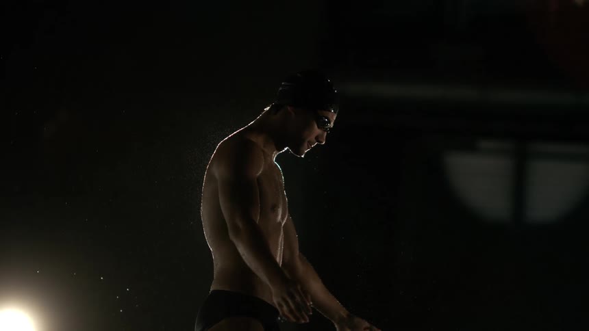 After a swimming session a swimmer wearing goggles and a cap flexes