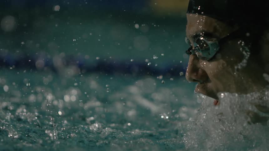 A swimmer in propels through a pool water splashing around as their arm cuts through the water