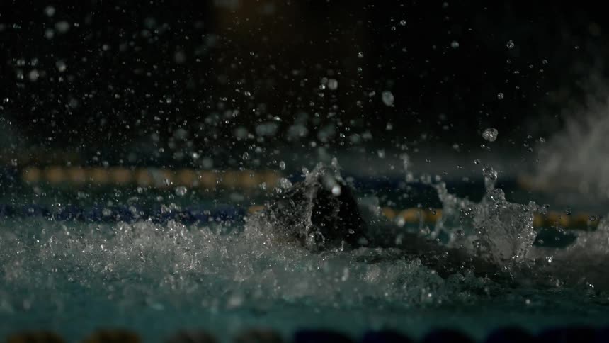 A person is doing the butterfly stroke in a pool and making a splash in the water when his arm enters the water