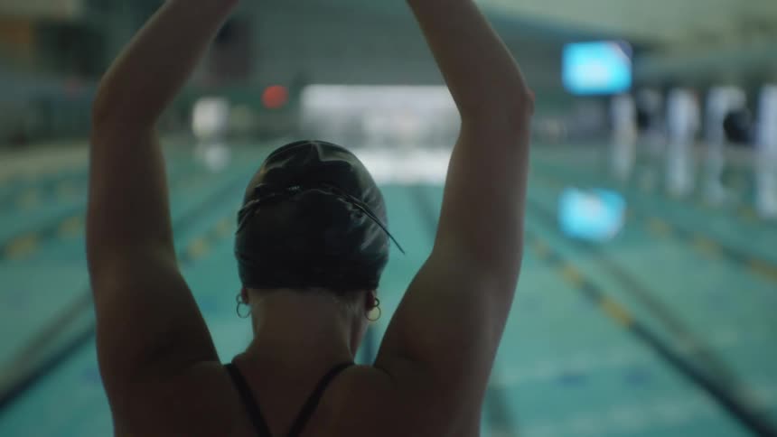 Back of a swimmer wearing a cap preparing to dive in a swimming pool