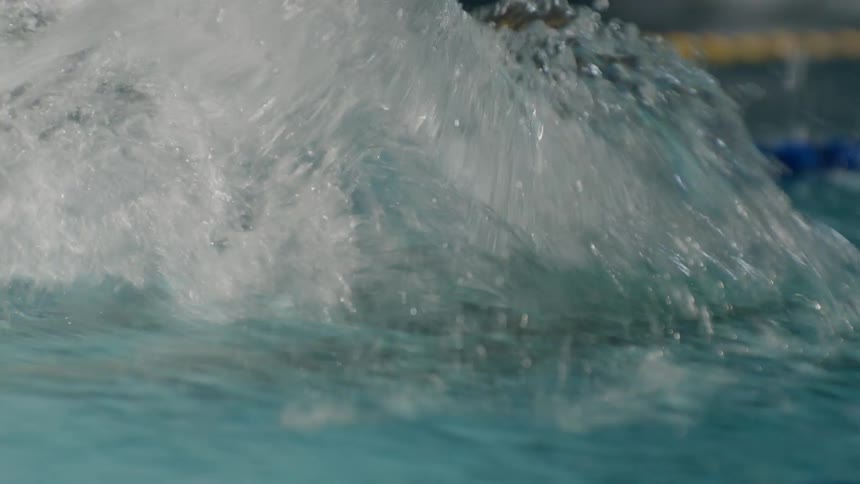A swimmer in propels through a pool water splashing around as their arm cuts through the water
