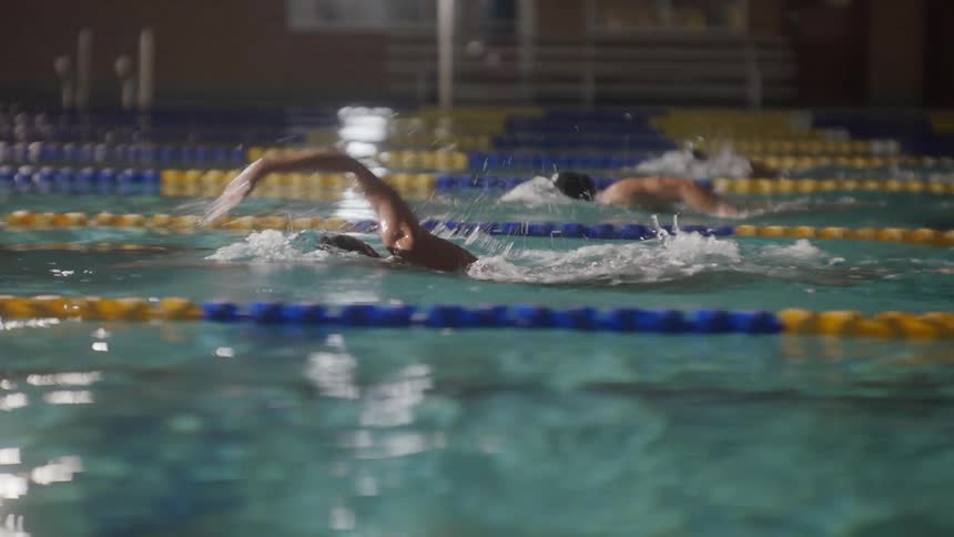 Swimmers competing in a pool with water splashing as they propel themselves through the lanes