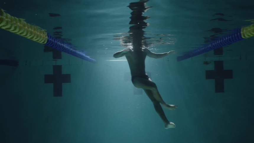 A closeup view of a person swimming underwater in a pool viewed from below