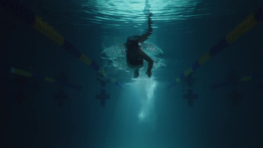 A view of a person swimming underwater in a pool viewed from below
