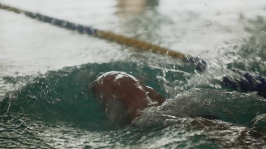 A swimmer in propels through a pool water splashing around as their arm cuts through the water