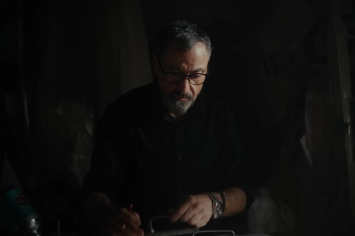 A man drawing over large sheets of brown paper on a dimly lit workshop