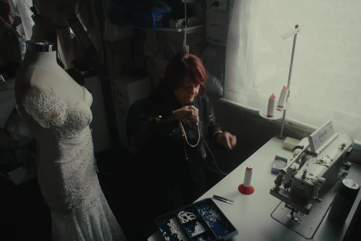 Dressmaker threads a needle in preparation for applying beads to dress
