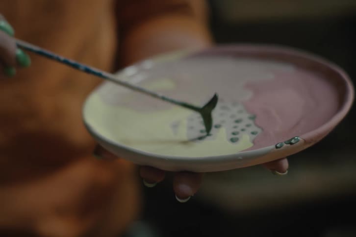 Woman decorates a shallow plate the size of her hand with paint