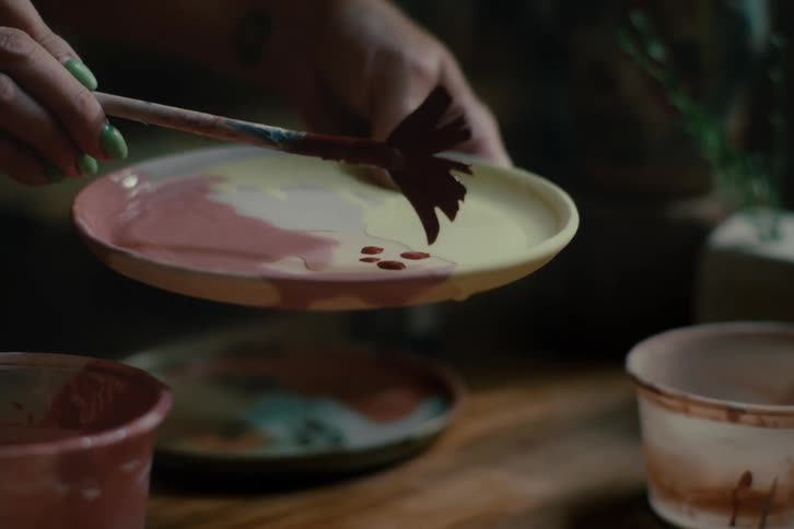 An artist is painting a clay dish with a worn out brush