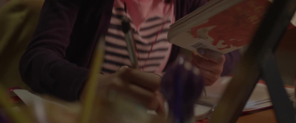Someone is reading a book and writing down notes with a pen