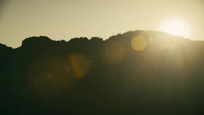 The sun rises over a forested mountain