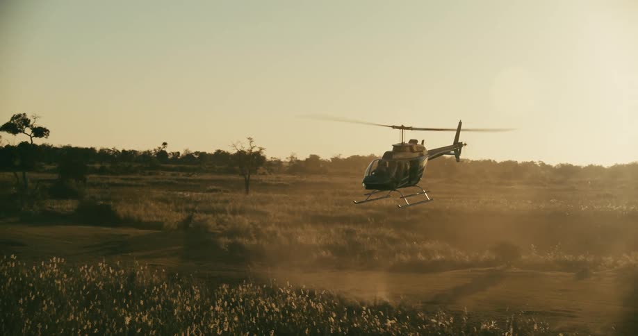A helicopter kicks up dust as it takes off from a clearing on a grassy plain