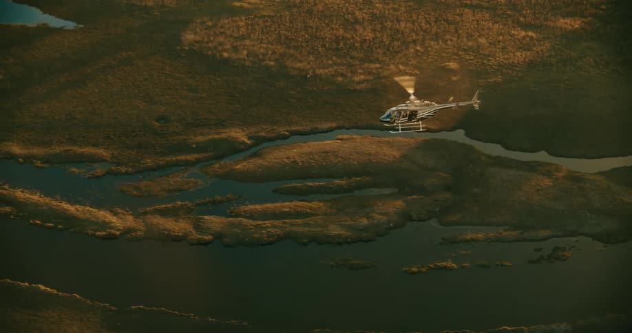 A helicopter flies over a river near a plain