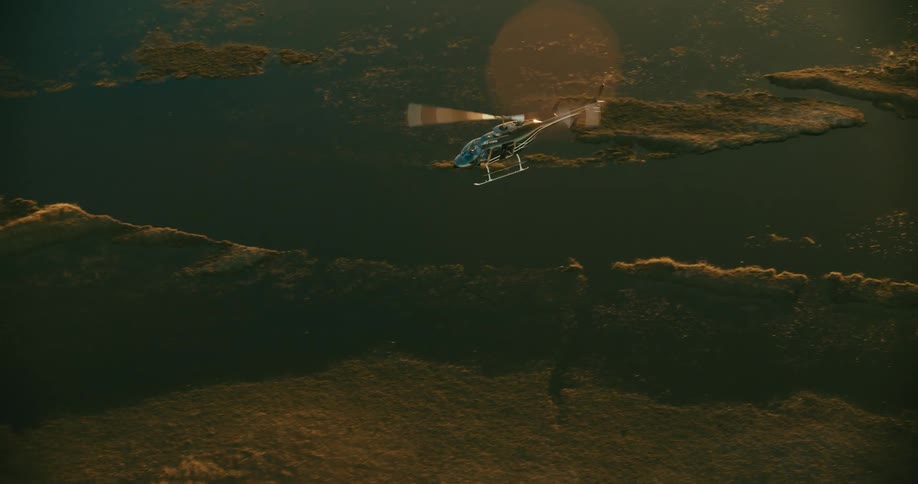 A helicopter flying over a savanna with a lake