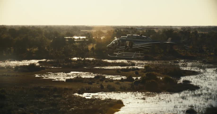 A white helicopter flying over a marshy area with water on the ground