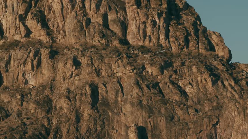 A helicopter flies in front of a giant mountain cliff