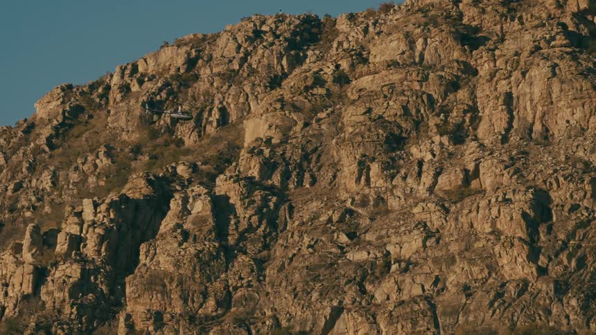 A helicopter flying over a huge rocky mountain on a clear day