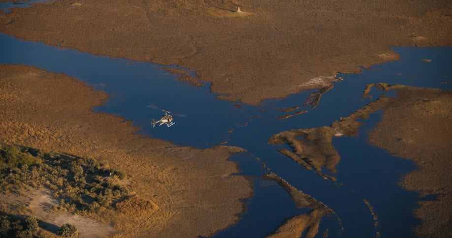 An aerial view of a river winding through a vast dry landscape with a helicopter visible