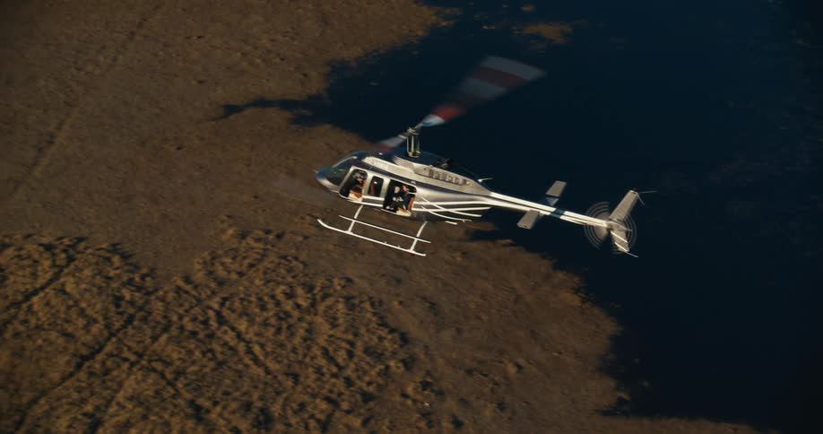 A white helicopter flying over a savannah with beige soil