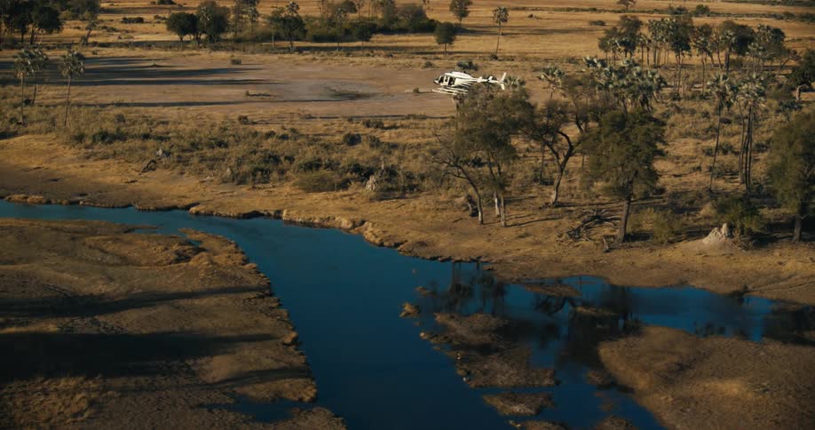 Helicopter flying above a winding river surrounded by dry land and sparse vegetation