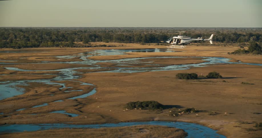 Aerial shot of a helicopter flying over a savanna with a river and forest